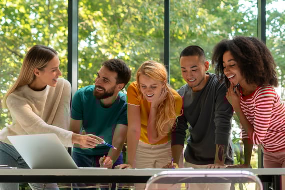 Un groupe de jeunes souriant autour d'une table où est disposé un ordinateur.
