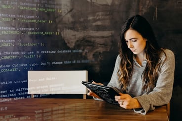 Jeune cheffe de projet IA assise à une table en train d'utiliser une tablette avec en surimpression sur la gauche de l'image des lignes de code.