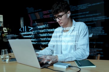 Un développeur junior code sur un ordinateur portable, il y a des lignes de code en surimpression au centre de l'image.
