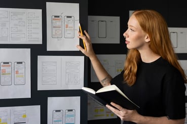 Jeune UX/UI Designer tenant un carnet de note et présentant des wireframes mobiles d'une futur page web.