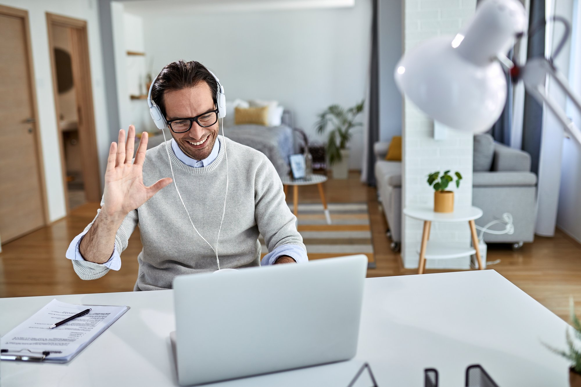 young-happy-businessman-waving-while-having-online-meeting-laptop-from-home